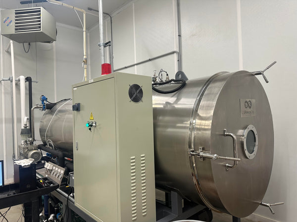 Industrial, commercial freeze dryer equipment with large metal tank and control panel in a room.