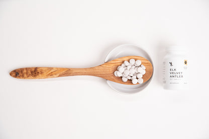 Wooden spoon with white capsules on a white background, next to a white supplement bottle.