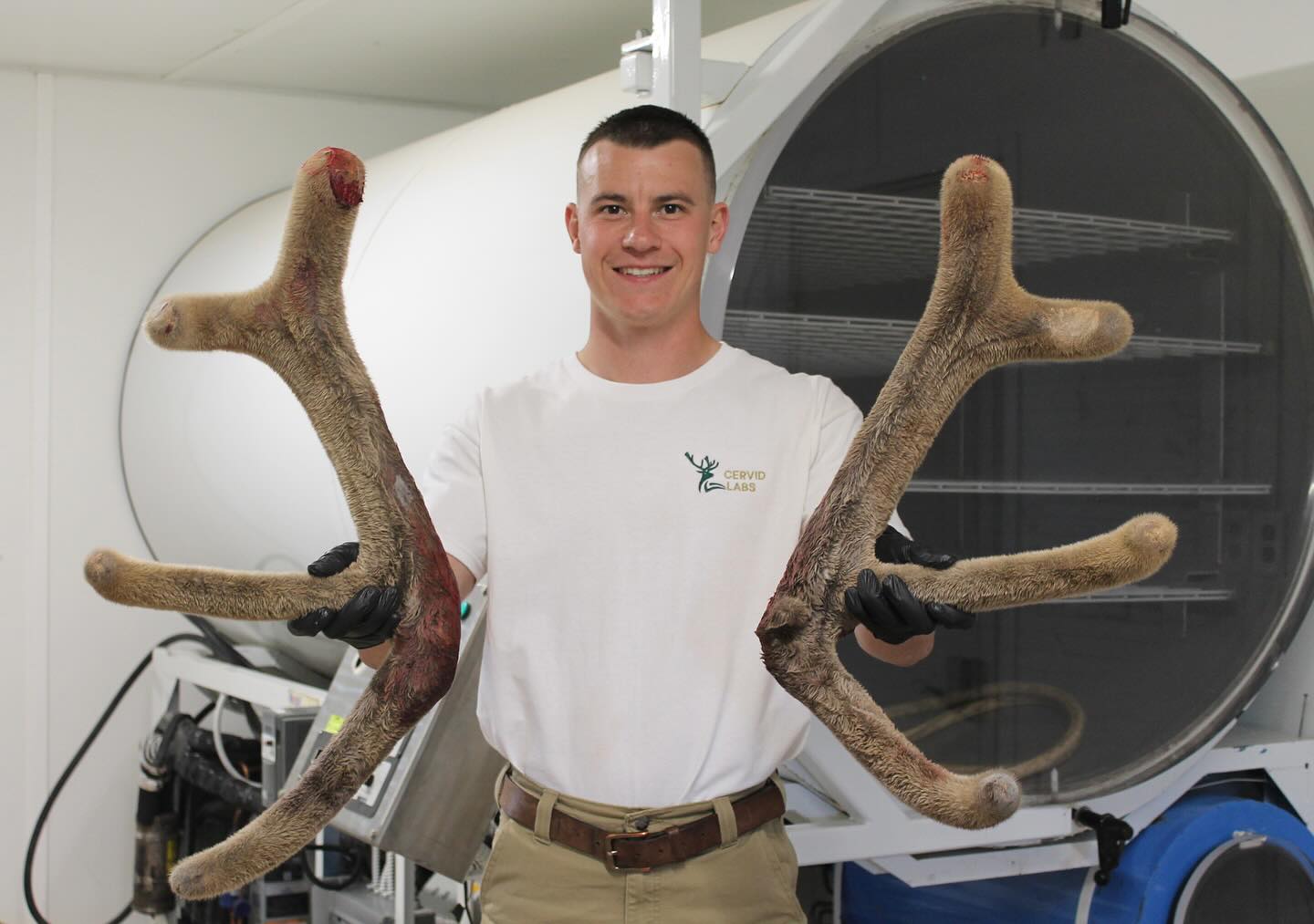 Man holding large elk antlers in front of a large vacuum chamber machine